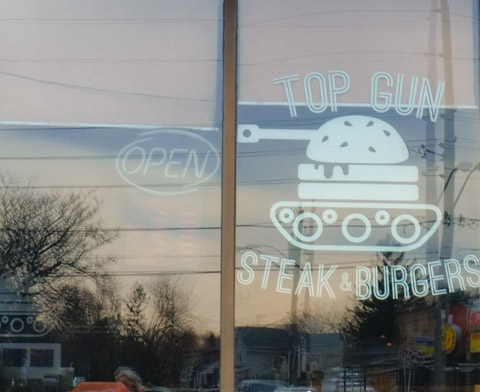 looking in window of top gun steak and burger restaurant, logo is a tank with the bod of the tank is a hamburger