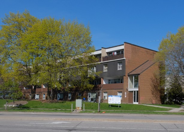 brick townhouse row with a blue and white development notice in front, Don Mills Road, St. Dennis Drive