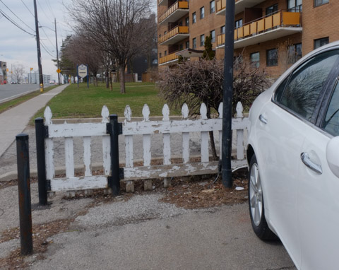 old low beat up white picket fence between parking lot and low rise apartment building