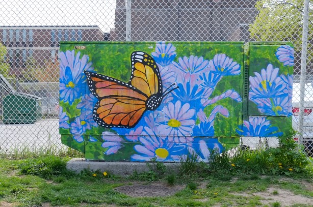metal box on sidewalk, bell box, painted with a monarch butterfly in a field of pale purple daisies