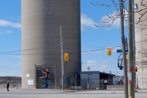 large photograph of a man transplanting plants and trees, in an orange vest, on the door of a silo