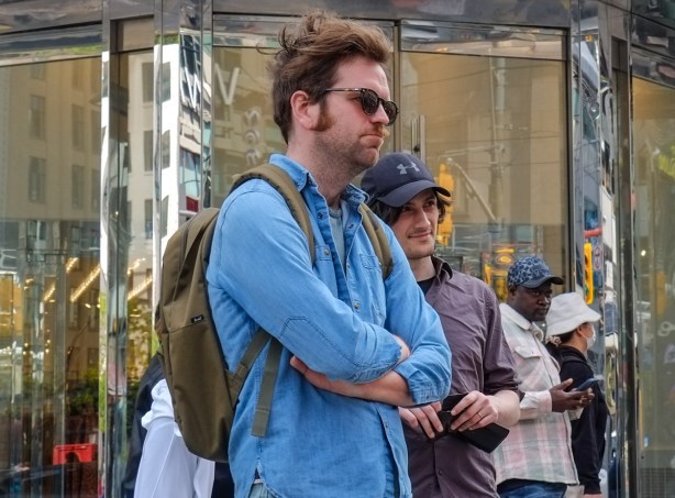 four men standing on the sidewalk watching a street performer