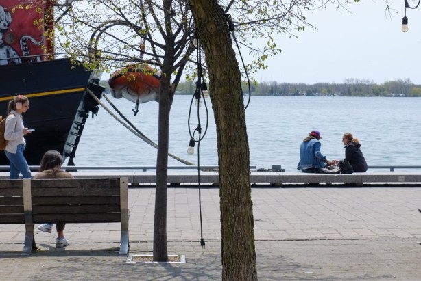 two people sitting on a bench by the waterfront, beside boat with a lifeboat