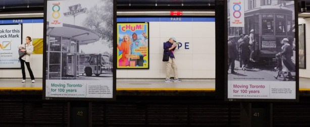 people waiting on the platform of pape station, with posters of history of ttc on display