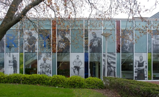 part of exterior wall of Cedarbrae library, part window and part photography exhibit, large photos in black and white of people