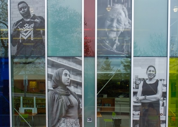 four large black and white portraits on exterior wall of glass windows Cedarbrae library, Resilience for ArtworxTO