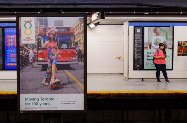 photo on display at pape subway station, from 2008, first Pride bus at Pride parade in Toronto, a woman in colourful clothes is walking in front of the bus