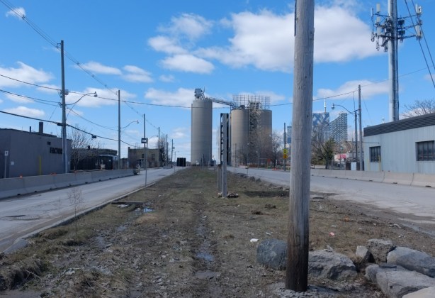 looking west along Villiers street to the large Lafarge cement silos at the end of the street, dirt and puddles in the median between the two lanes of traffic, a divided road