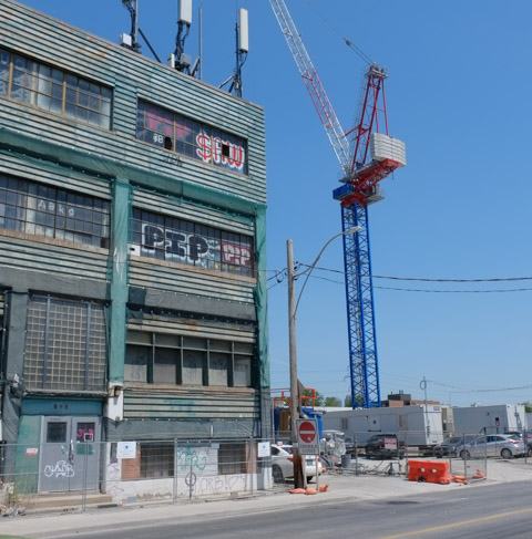 tall blue crane on construction site next to glass industrial warehouse building from 1921 at 888 Dupont street 