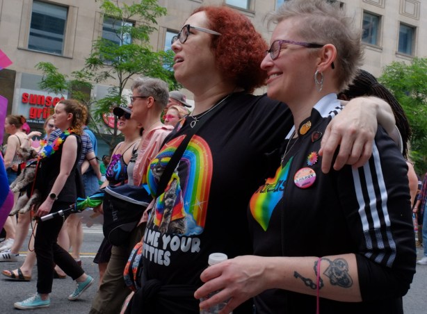 women in dyke march along Bloor street in Toronto, red head younger woman with her arm around the shoulders of an older woman