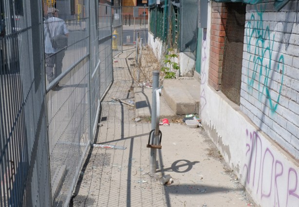 outdoor sidewalk space, narrow, between old building and construction fence