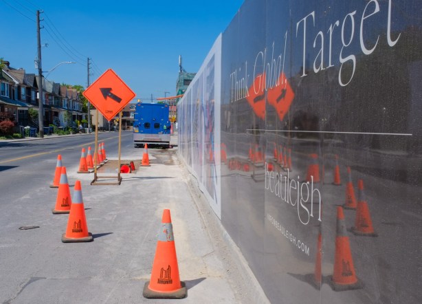 shiny hoardings around a construction site reflect the bright orange signs and cones on the street beside it 
