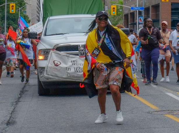 people walking in dyke March, woman dancing in front of a white vehicle