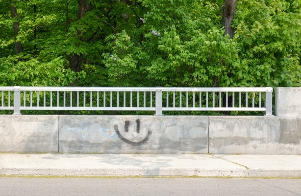 concrete wall on bridge, has a black happy face spray painted on it
