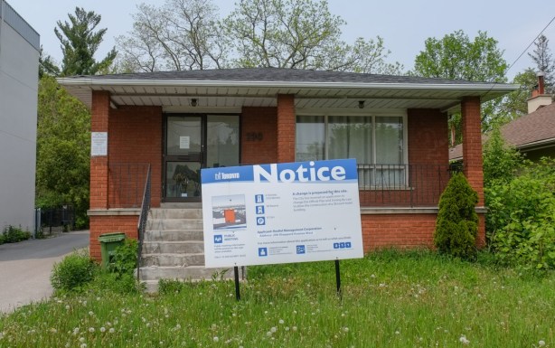small brick bungalow with development notice in the front yard