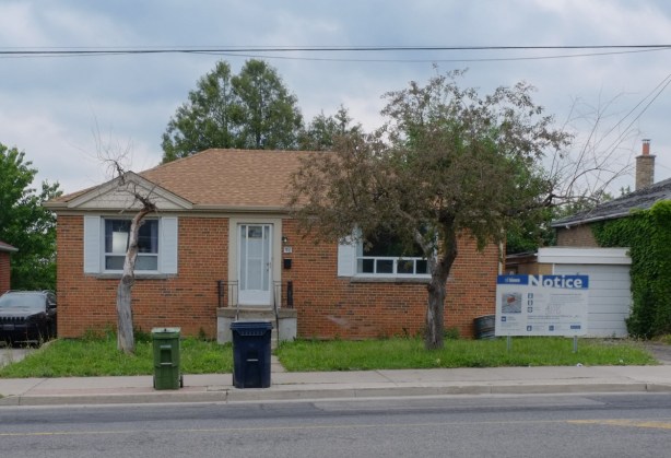 small brick bungalow with a blue and white development notice in the front yard