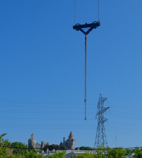 blue sky with chain from crane (not in picture) hanging in the foreground, a large metal utility tower in the middle, and the top of Casa Loma roofline in the distance