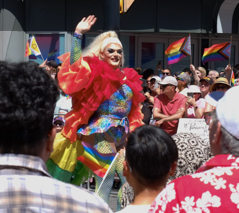 man in drag in pride parade, sequin dress, red jacket, 