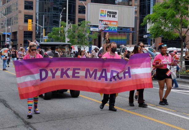 dyke march, pride toronto, purple, pink, and orange striped banner that reads dyke march