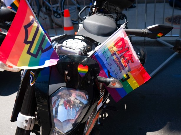black motorcycle decorated for pride parade, rainbow flag with words written on it that say dyke on bike, pride was a riot 