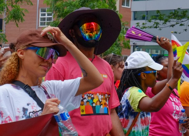 people walking in dyke March, one with large reflective mask on as well as black hat