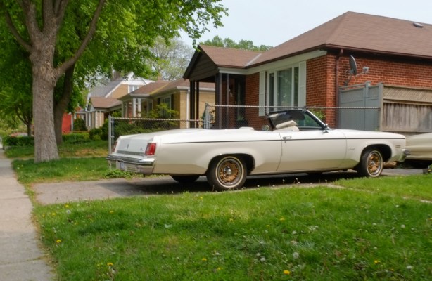 old white convertible with top down parked in driveway in front of a house