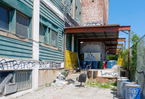 side of a an empty building at 888 Dupont waiting for demolition, small space beside building with old chairs and other junk under a steel beam overhang