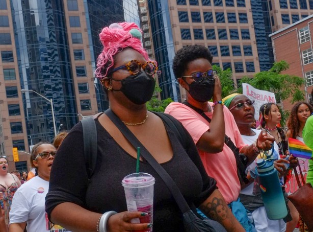 people walking in dyke March including a black woman with long braids in black and pink tied up on the top of her head, 