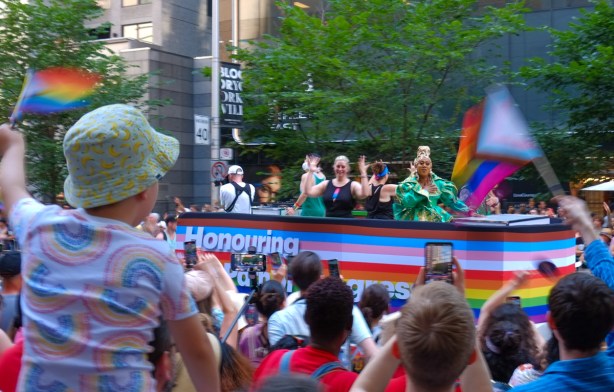 people waving small rainbow flags as a float passes by 