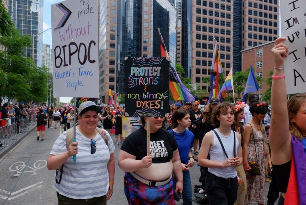 group pf women at dyke march in downtown toronto, carrying signs, one says no pride without bipoc and the other says protect trans rights