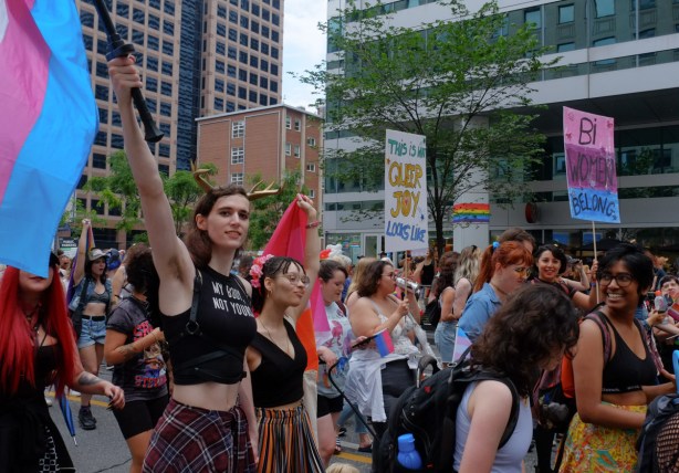 dyke march, pride toronto, woman with flag held up high, placard that reads this is what queer joy looks like 