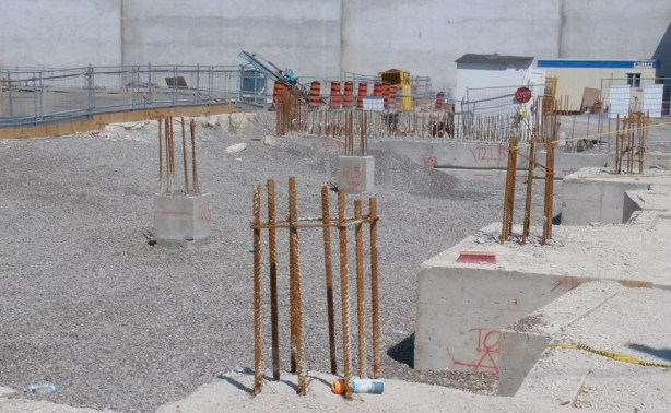 rebar sticking out the ground, construction site, as building begins to rise from the ground
