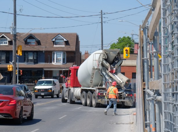 workman helping a concrete truck back up into a construction site, traffic waiting, 