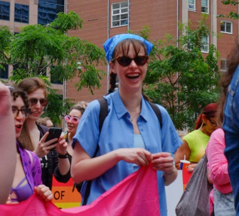 dyke march parade, young woman in blue, dark sunglasses and blue kerchief, smiling