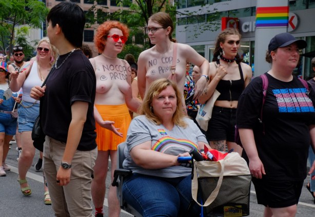 group pf women at dyke march in downtown toronto, two are topless, with no cops at pride written on chest another is in a wheelchair