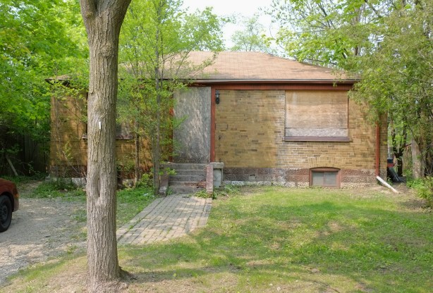 old brick bungalow with boarded up windows and door