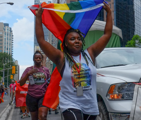 people walking in dyke March, walking beside a white vehicle, a woman carrying a rainbow flag above her head