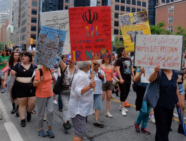 women walking in dyke march, carrying anti Islamic regime signs, signs with women, life, freedom