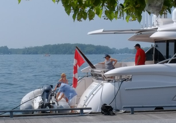 people on the back of a large boat, looking at man working on smaller boat moored beside it