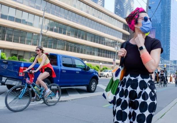 two women, one on a bike by a blue truck, on in red head scarf and black and white polka dot skirt, 