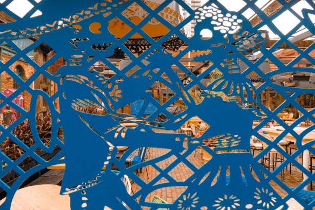 looking through a blue metal cutout of a mexican day of the dead couple, to a restaurant on the other side