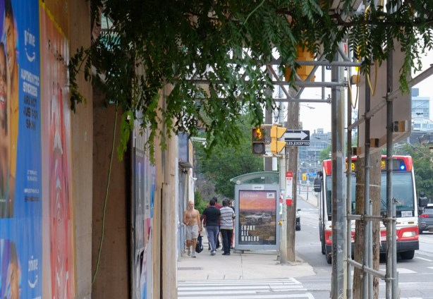 looking through scaffolding covering sidewalk to bus stop and people on the other side of the street 