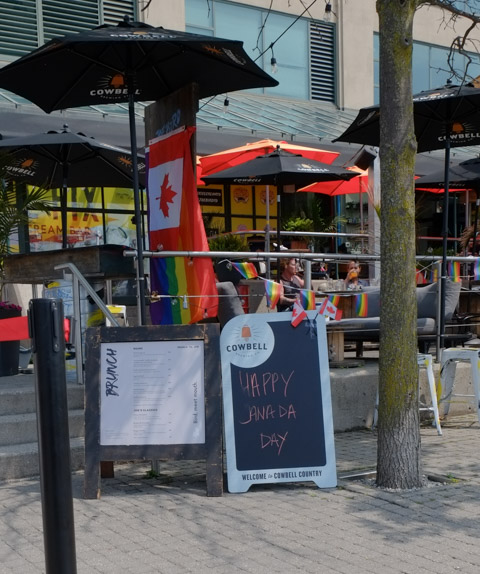 front of restaurant, patio, canadian flag, happy canada day sign, rainbow umbrella
