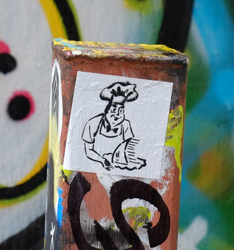 black drawing on white, man in chef hat holding a platter with what looks like a shark fin or a sailboat