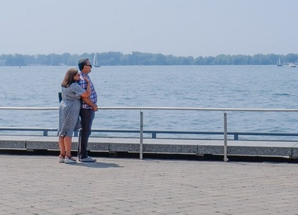 a couple stand together at the edge of the waterfront, by Lake Ontario