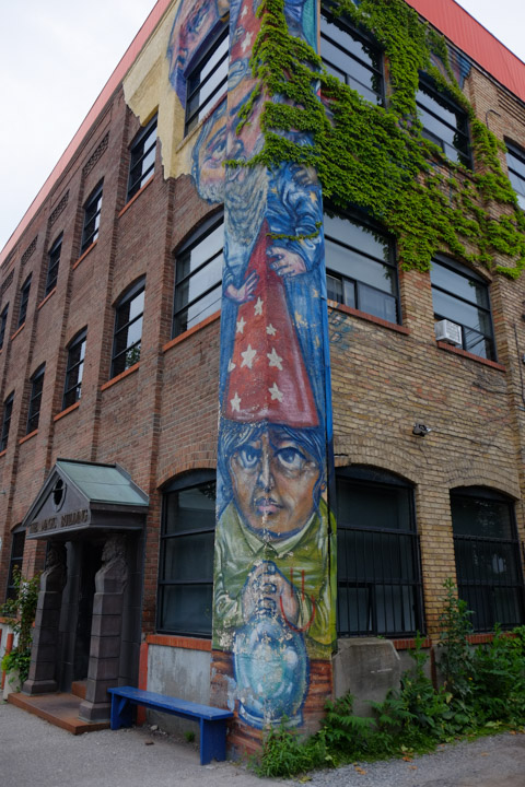 on the corner of a building, tall vertical mural by Elicser Elliott, a wizard in a red cap with white stars all over it. 