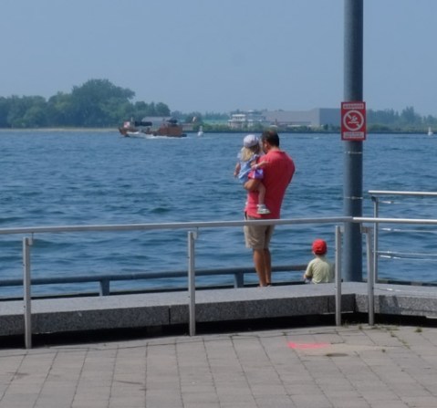 standing by Lake Ontario, a father holds a young child while another stands beside