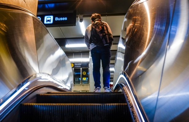 man with a backpack riding escalator at subway station, going up, reflections in metal sides of the escalator