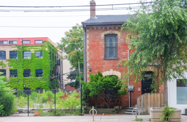 old brick house beside a vacant lot, building in next street behind can be seen, it is covered in ivy