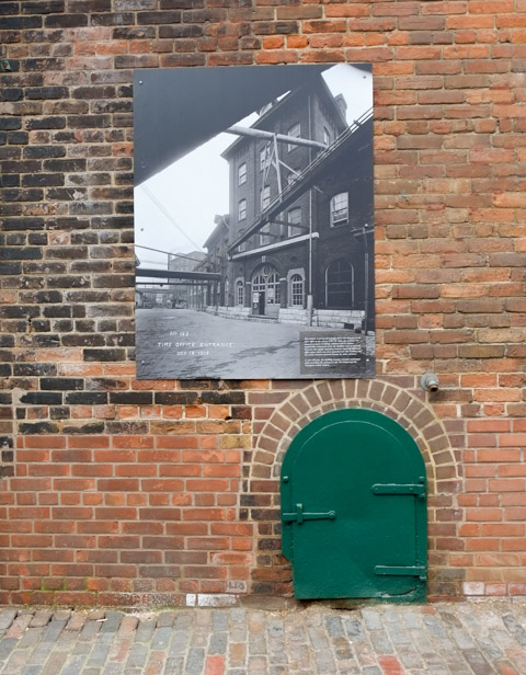 little green metal door in brick wall at Distillery, with a copy of an old black and white photo of a distillery building
